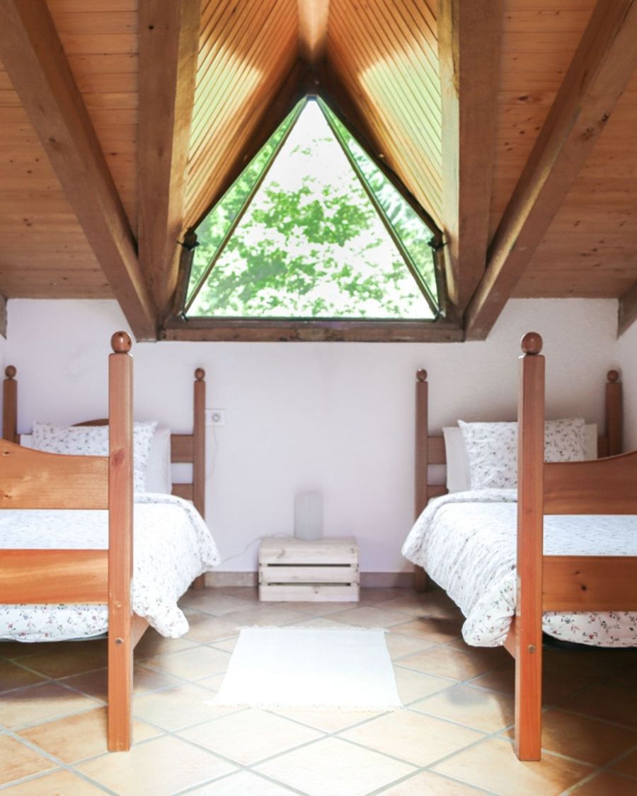 Habitación con dos camas bajo un techo de madera y una ventana triangular